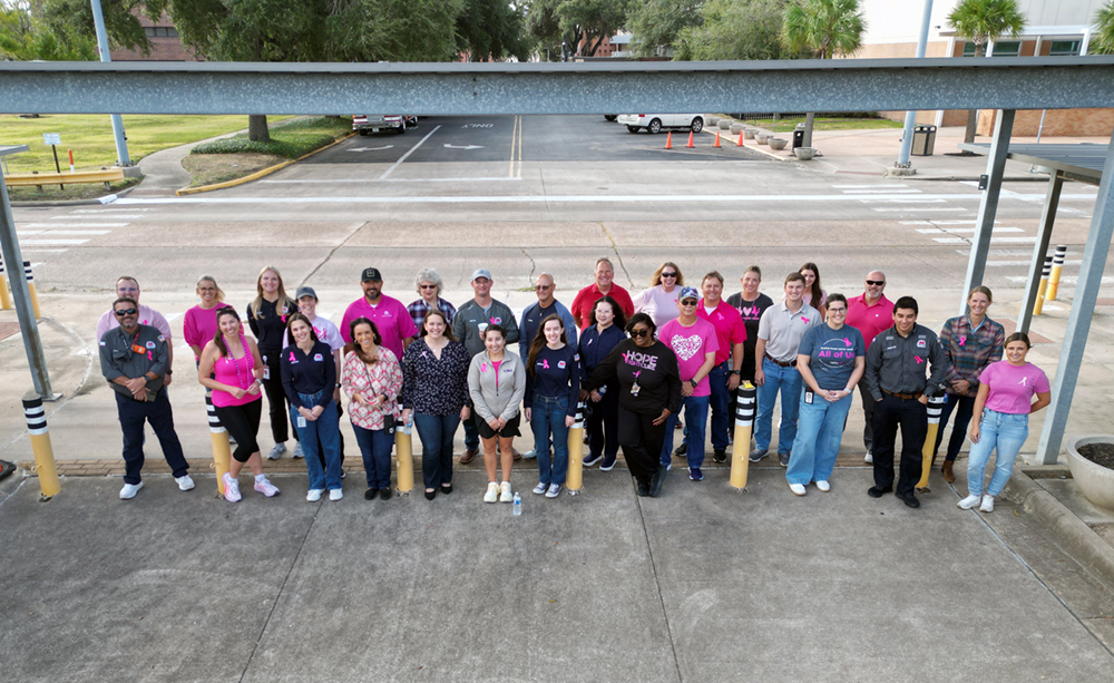 People standing together in a parking lot beneath a steel beam, with some individuals placing their hands together.