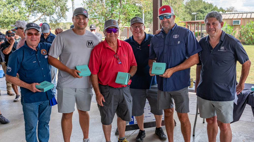 Six men standing together under a park shelter, smiling after an event and holding turquoise-colored boxes.