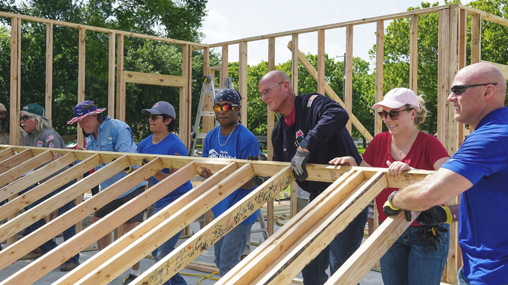 A group of people raising a wall frame at a construction site.