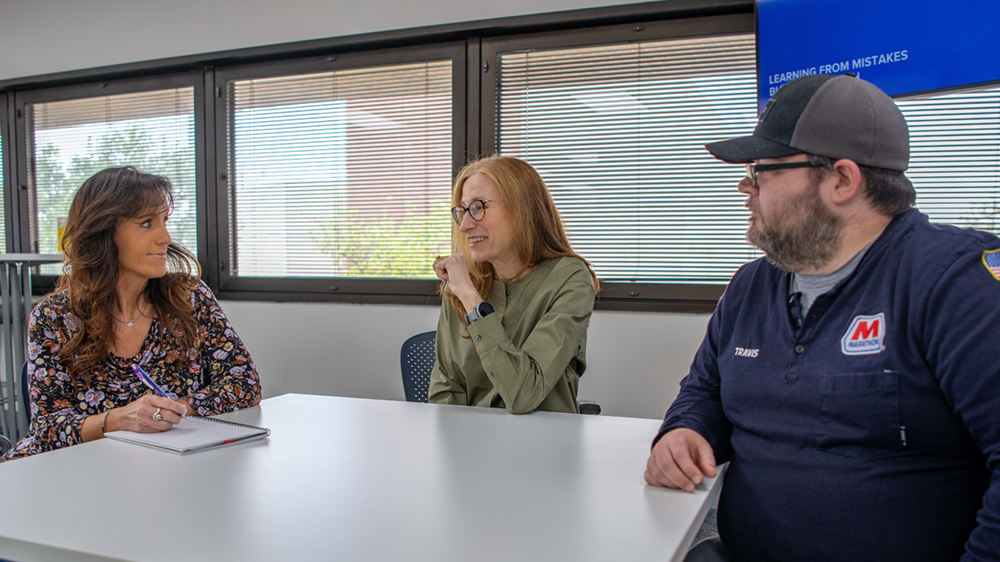 Three people sit and talk together at a table.