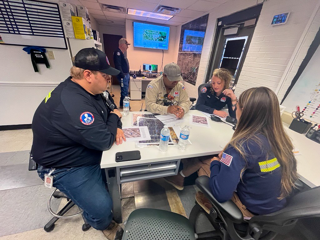 Four people sit at a table and look at papers with images on them.