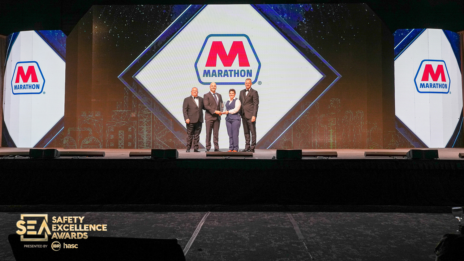Award recipients and presenters pose together on stage at an indoor awards ceremony.