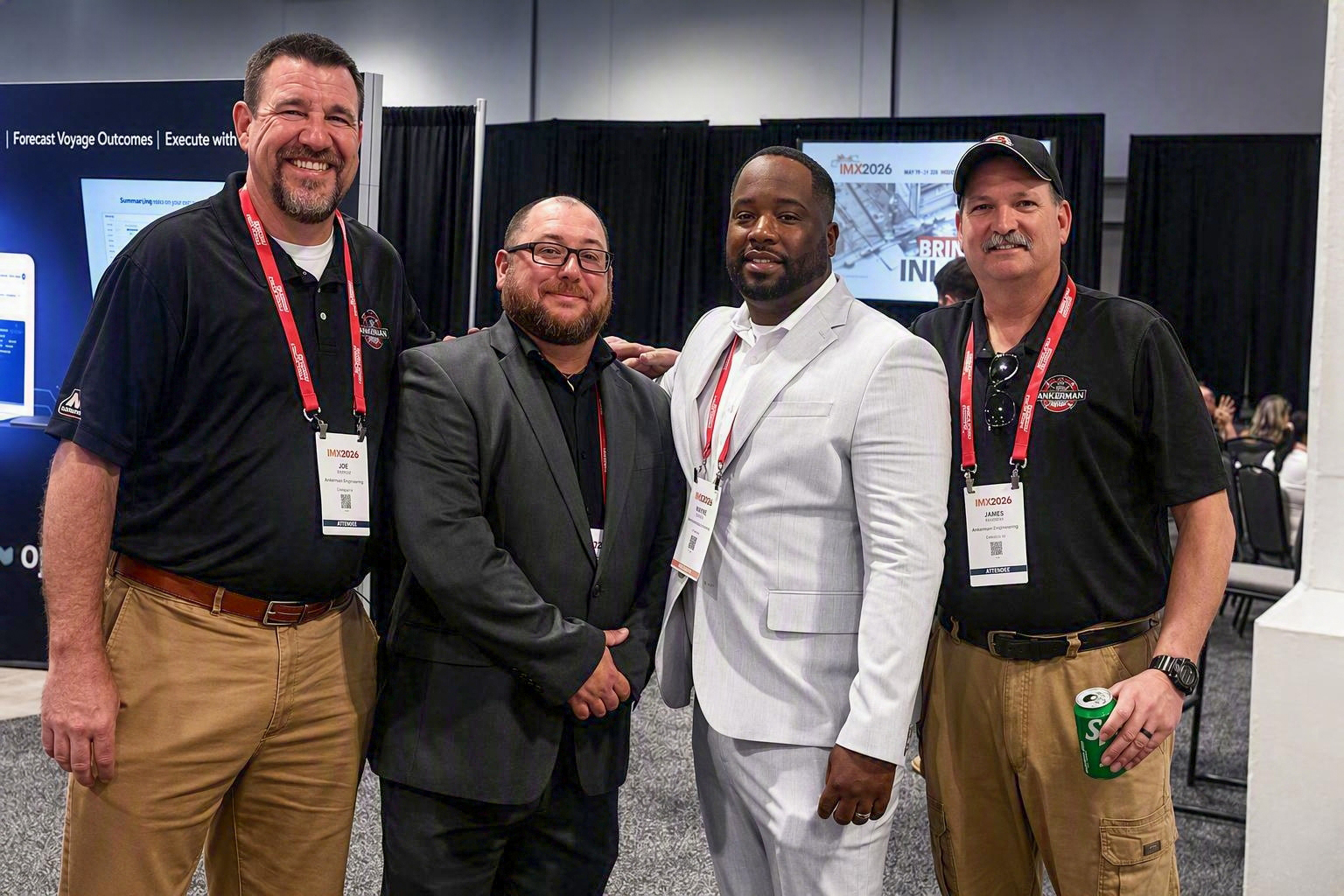 Four men wearing lanyards stand together at a conference.