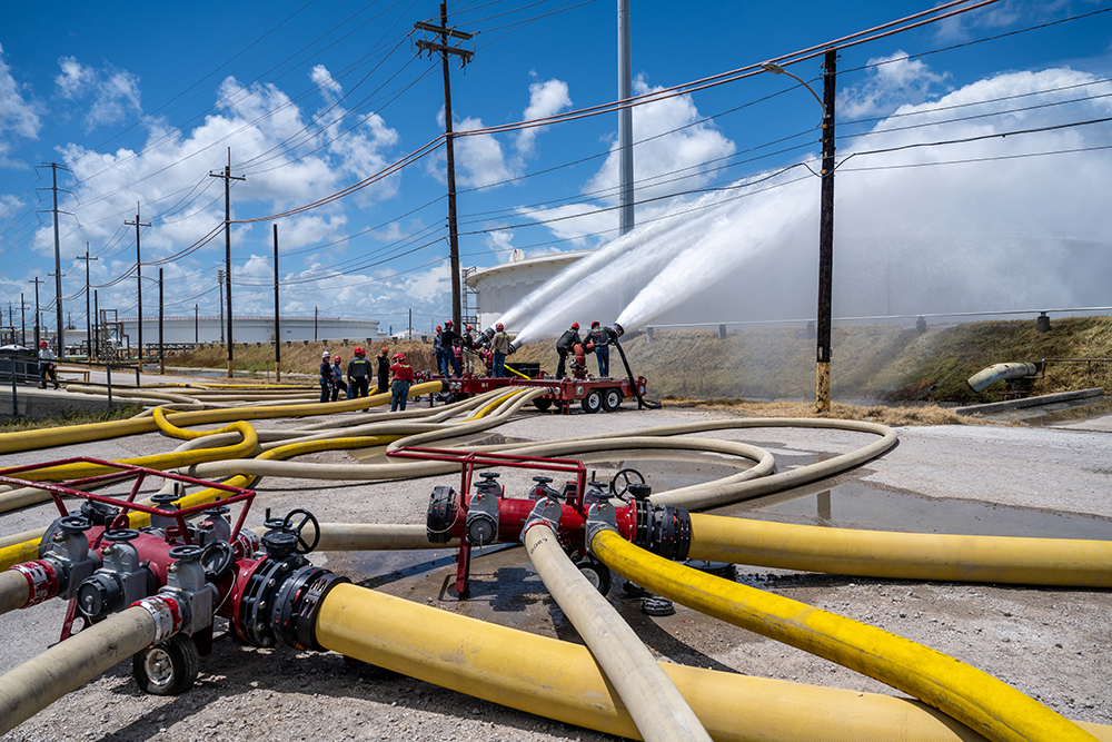 Emergency crews spray water from multiple large hoses during a full-scale emergency response drill at a refinery.