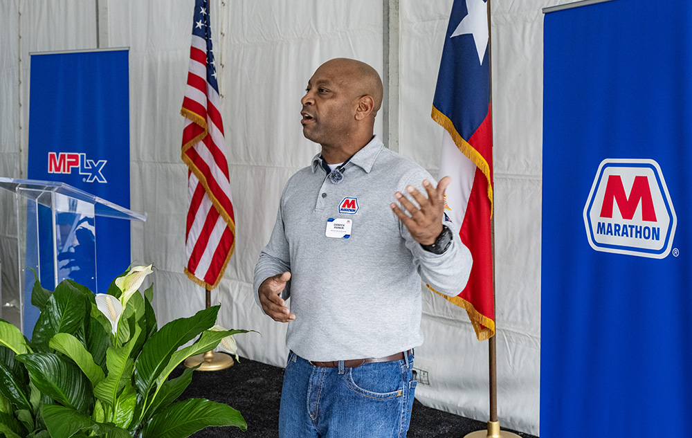 A man gesturing as he speaks while standing near a lectern. 
