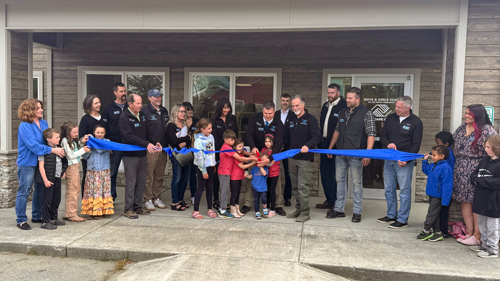A large group of adults and children behind a blue ribbon.