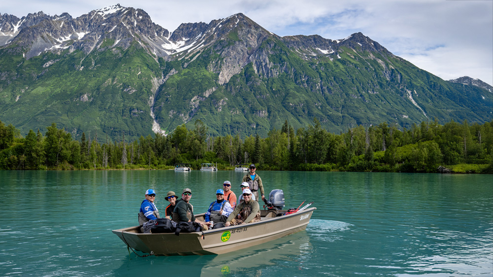People in a fishing boat on a lake with mountains in the background.