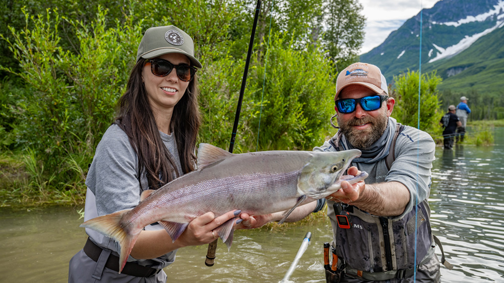 Two people holding a sockeye salmon while standing in the water.