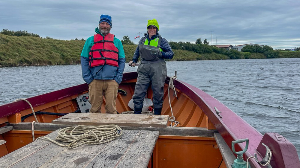 Two people stand in a boat in a lake.