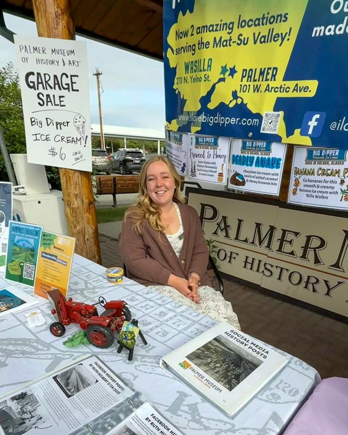 A woman sits at a table covered with maps and artifacts.