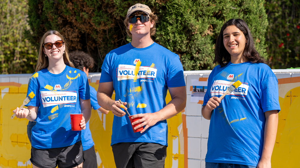 Three people in blue volunteer shirts hold paint brushes.
