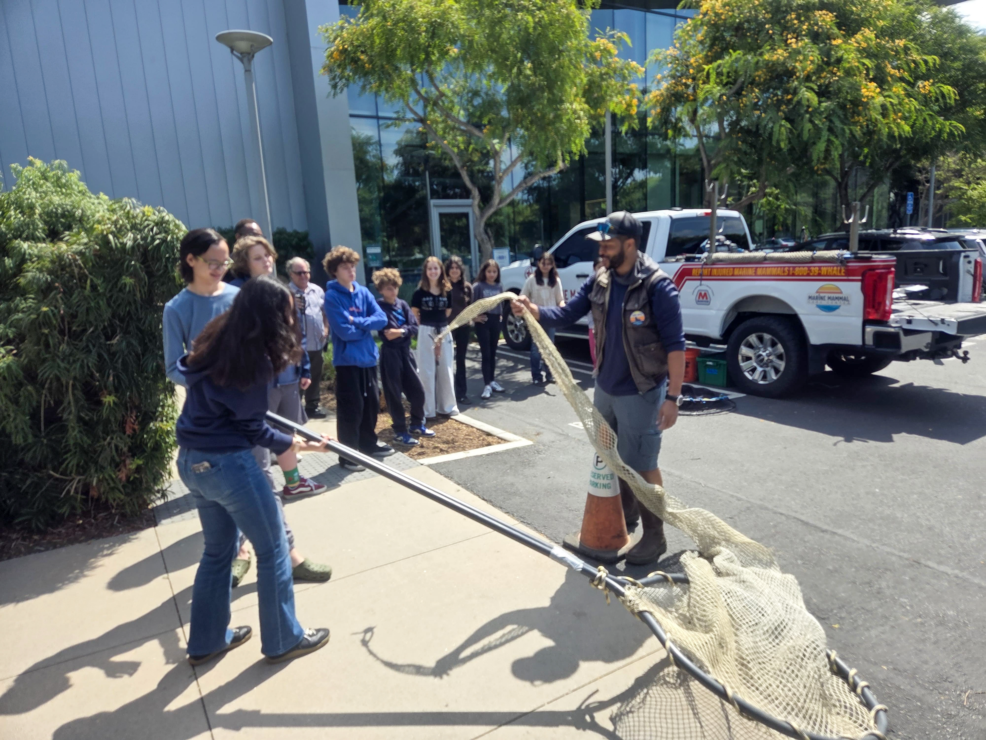 A group of people stand together holding a large net near a truck during an outdoor demonstration.