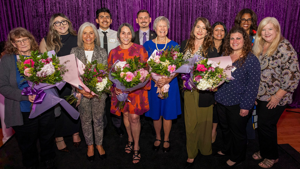 A large group of people posing for a photo at an event, with several holding flowers.