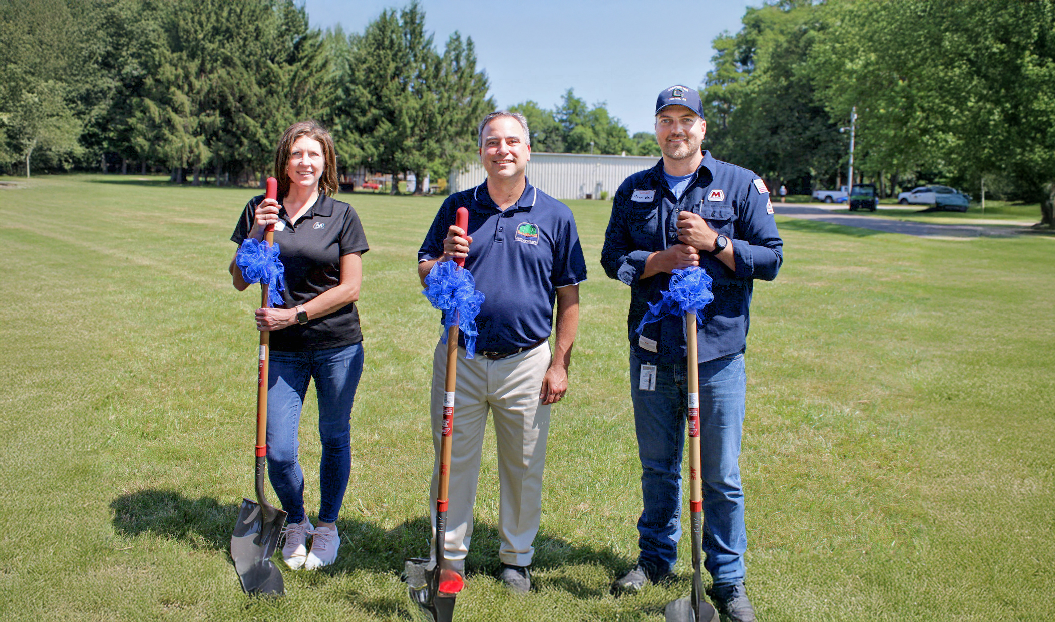 Three people each holding a shovel and smiling.