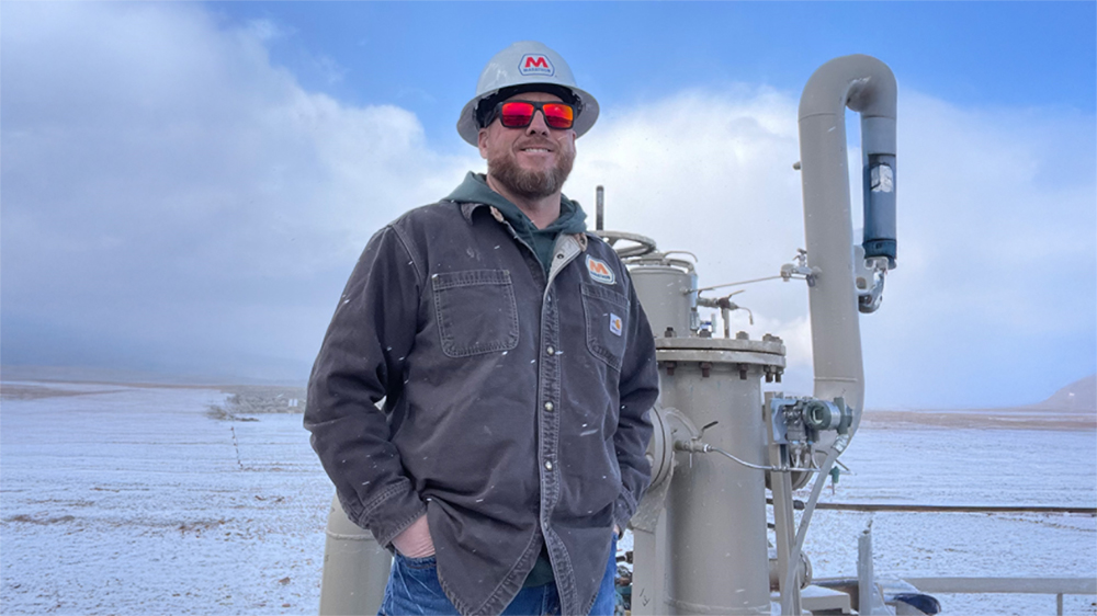 A man standing outdoors wearing work clothes and safety gear.