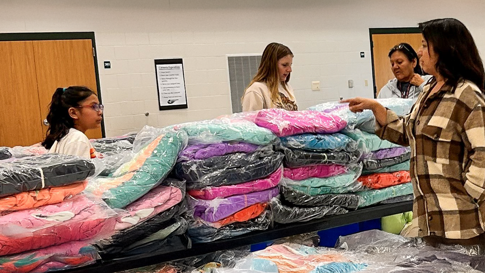 People standing next to a table of stacked coats. 