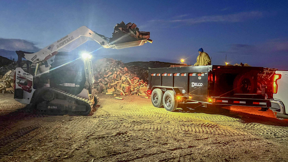 A piece of heavy equipment loads cut logs into a trailer.