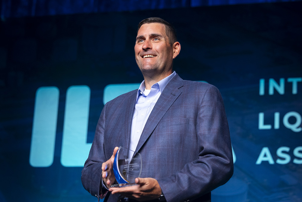 Man in a blue suit holds an award.