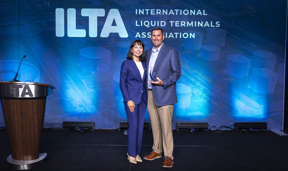 Two people stand together on stage with ITLA on a screen in the background.