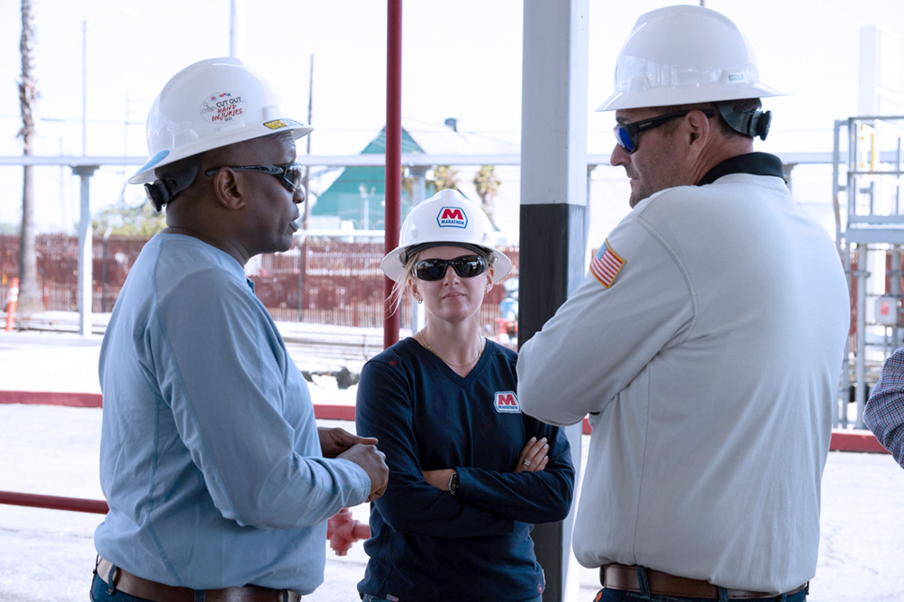 Three people in hard hats standing together in conversation.