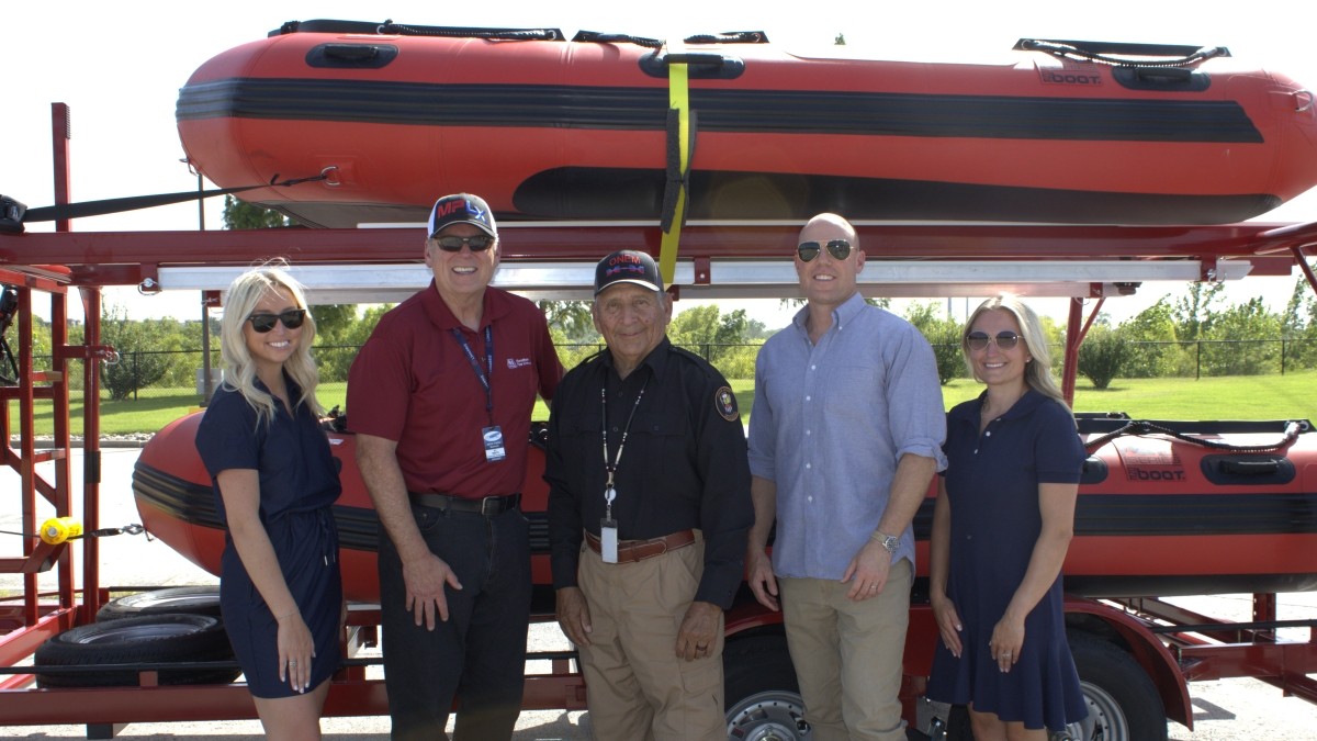 Five people standing in front of a trailer carrying rescue boats.