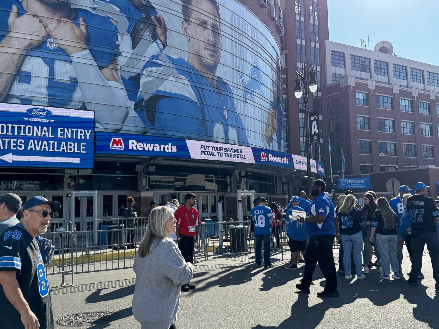 People in sports jerseys walk outside a brick building on a sunny day.