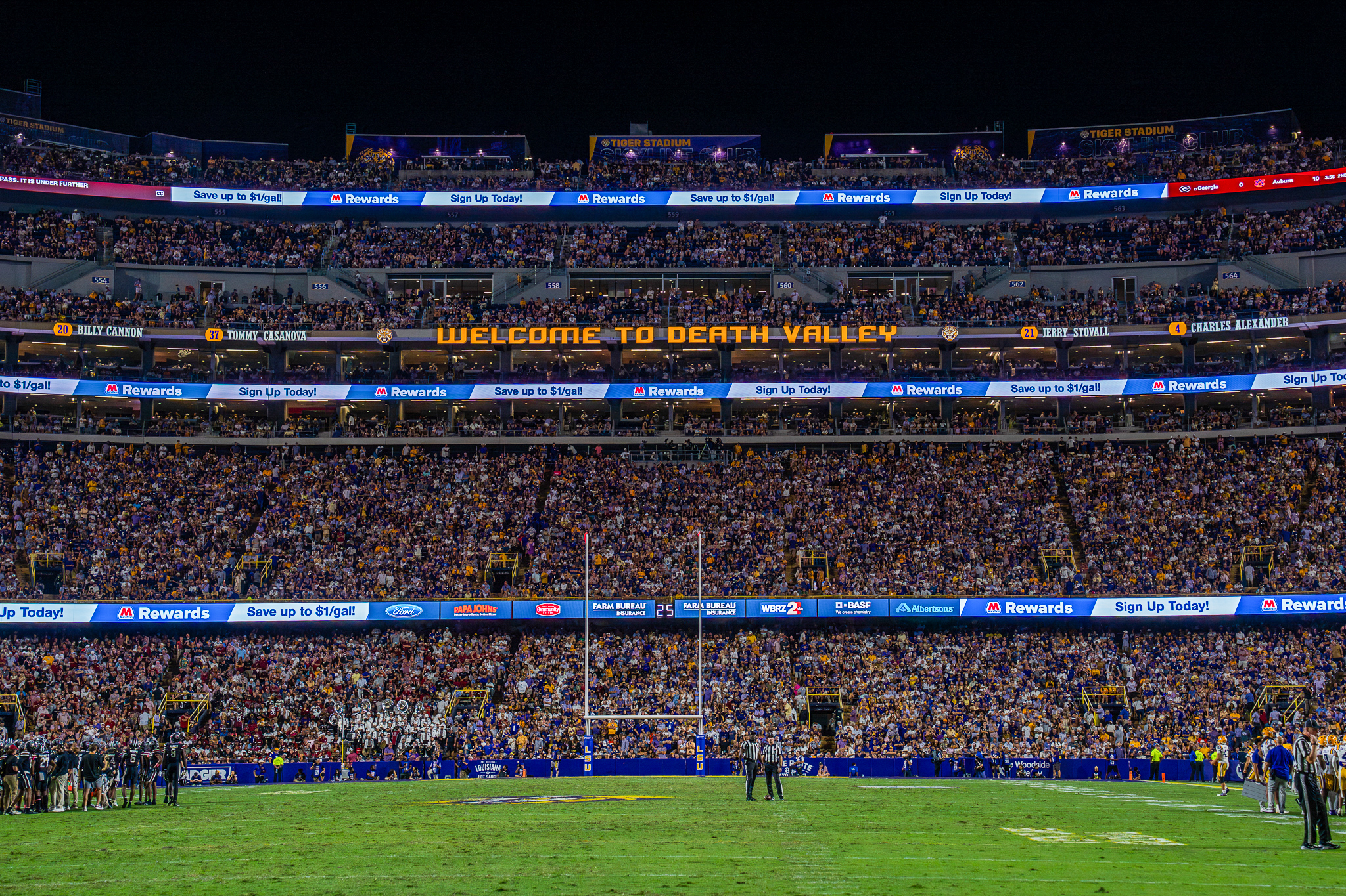 Inside a crowded sports stadium at night, with bright lights illuminating the seating and field.
