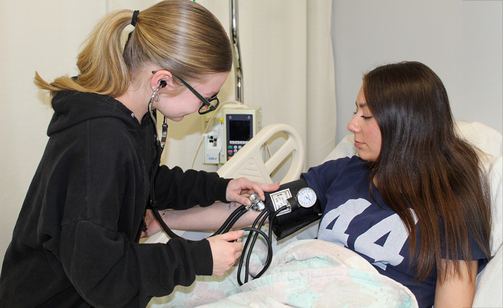 A student checks the blood pressure of another student. 