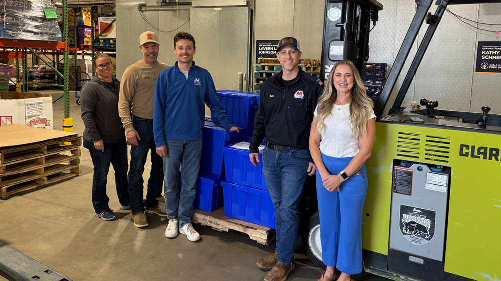 Five people stand together for a photo inside a warehouse facility.