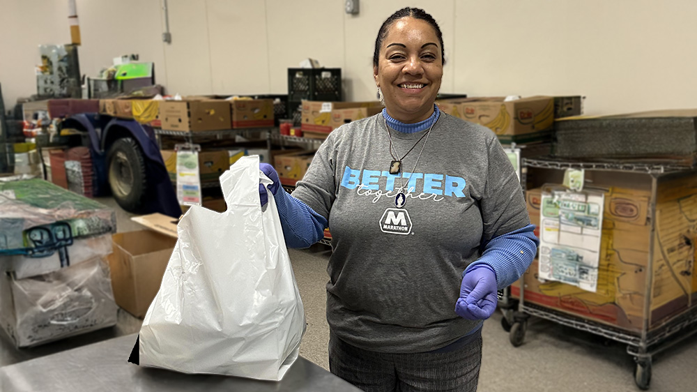 A woman wearing gloves holds a white bag of food with boxes behind her.