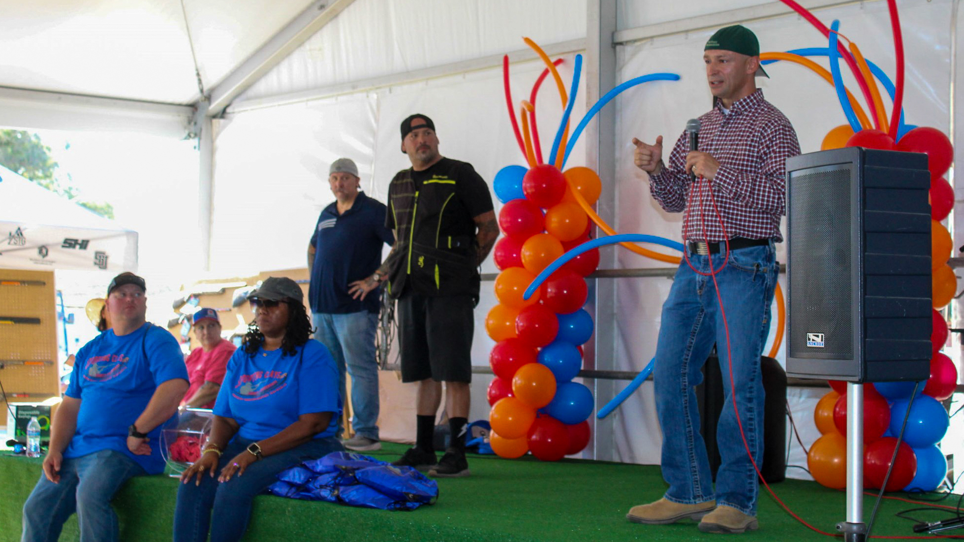 People on a green stage with colorful balloon decorations in the background. 