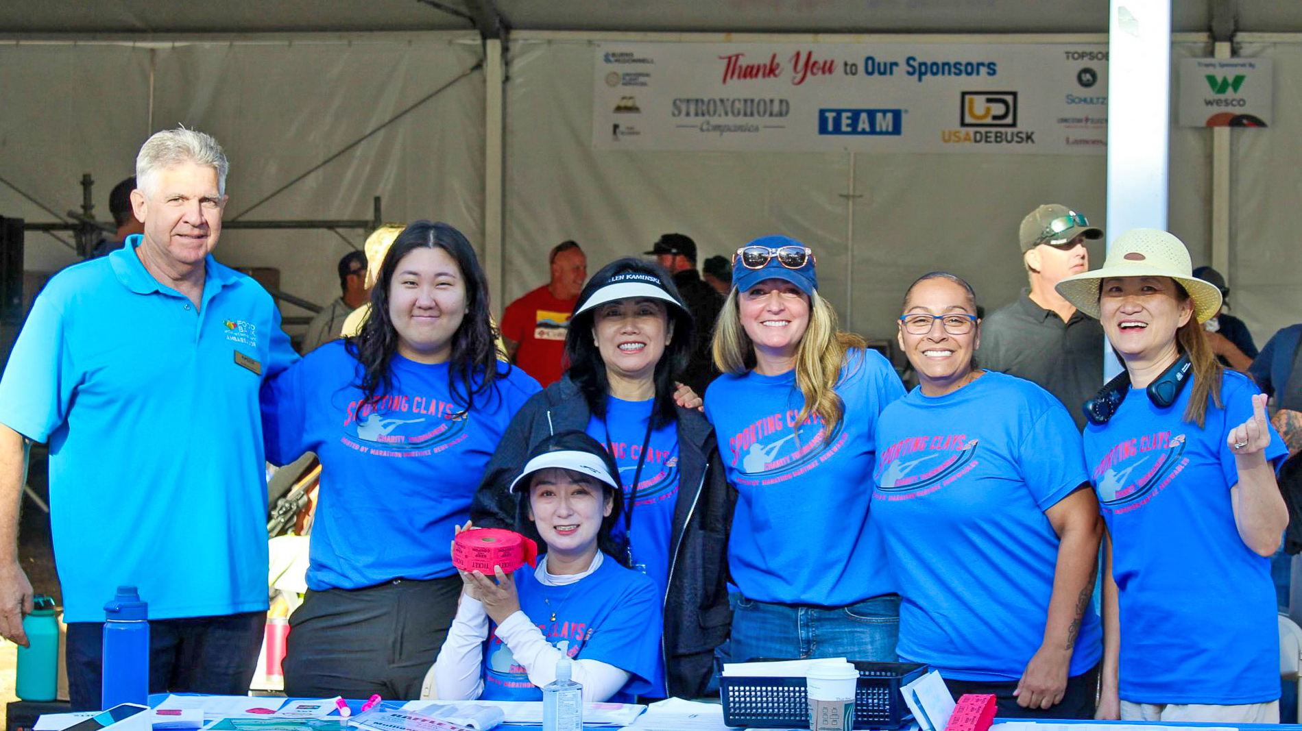 A group of people wearing blue shirts behind a table with red raffle tickets. A group of people wearing blue shirts behind a table with red raffle tickets.