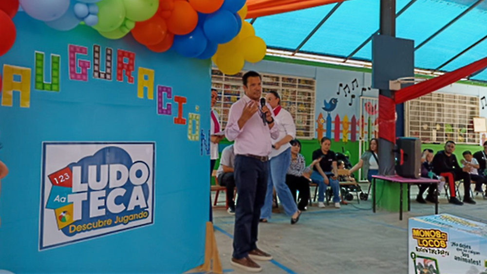 A man addresses a group of people while standing in front of a colorful display with a microphone.