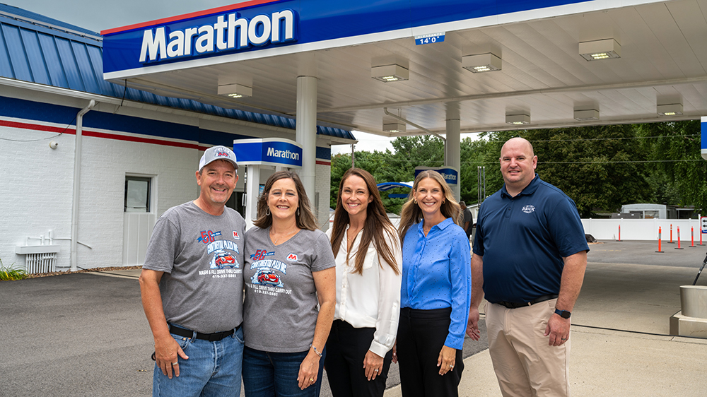  A group of people pose for a photo outside a gas station.