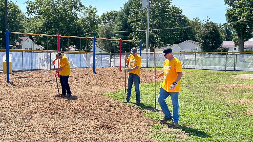 Employee volunteers spread fresh mulch across a school playground.