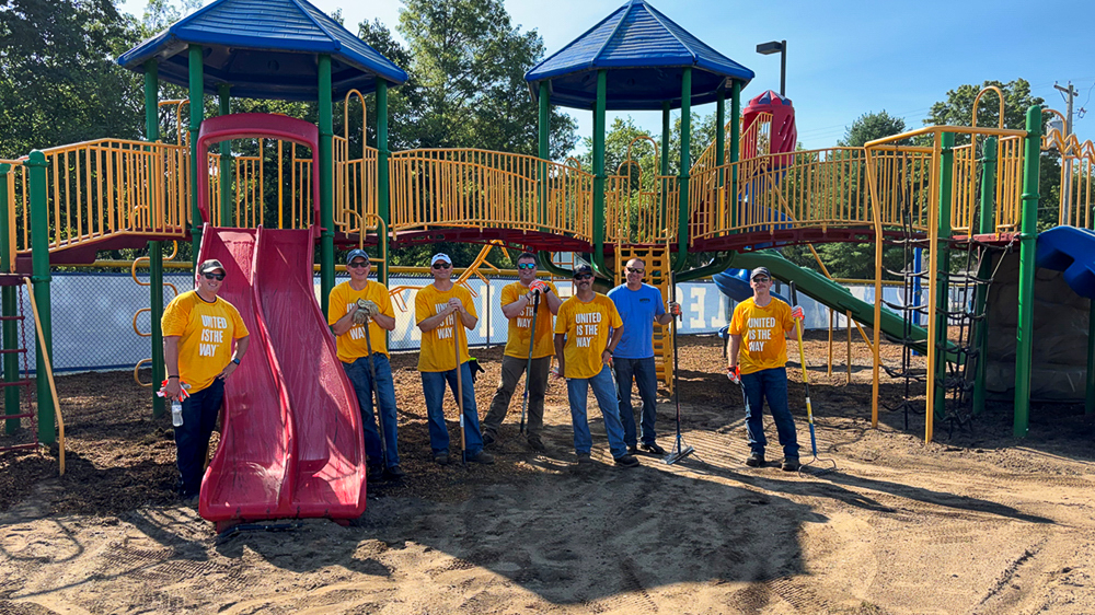 Seven employee volunteers stand together on a school playground after a community service event.