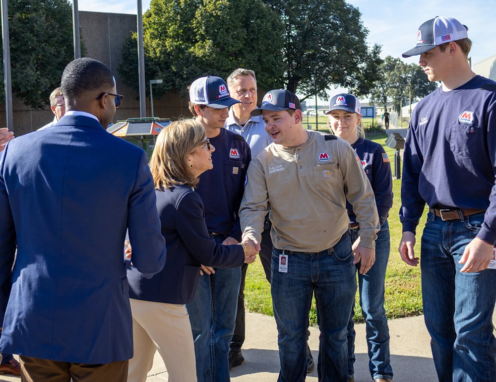 A group of people stand together and talk during an outdoor groundbreaking event.
