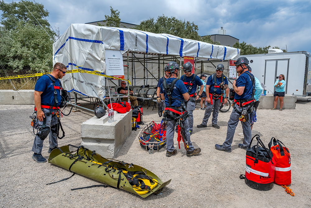 A group of men stand near pieces of rescue equipment arranged on the ground. 