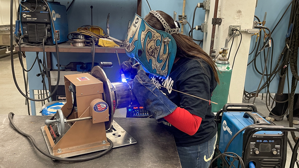 A young woman welds metal. 