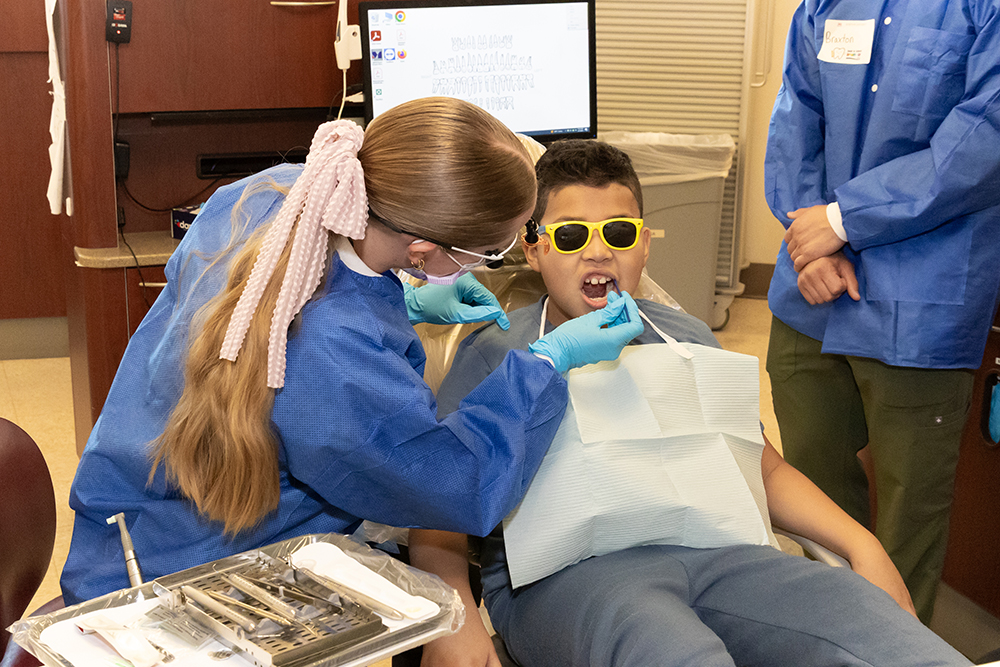A dental school student examines the teeth of a young boy in a dental chair.  
