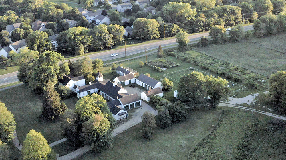 Aerial view of a farm with several white buildings surrounded by trees and grass.