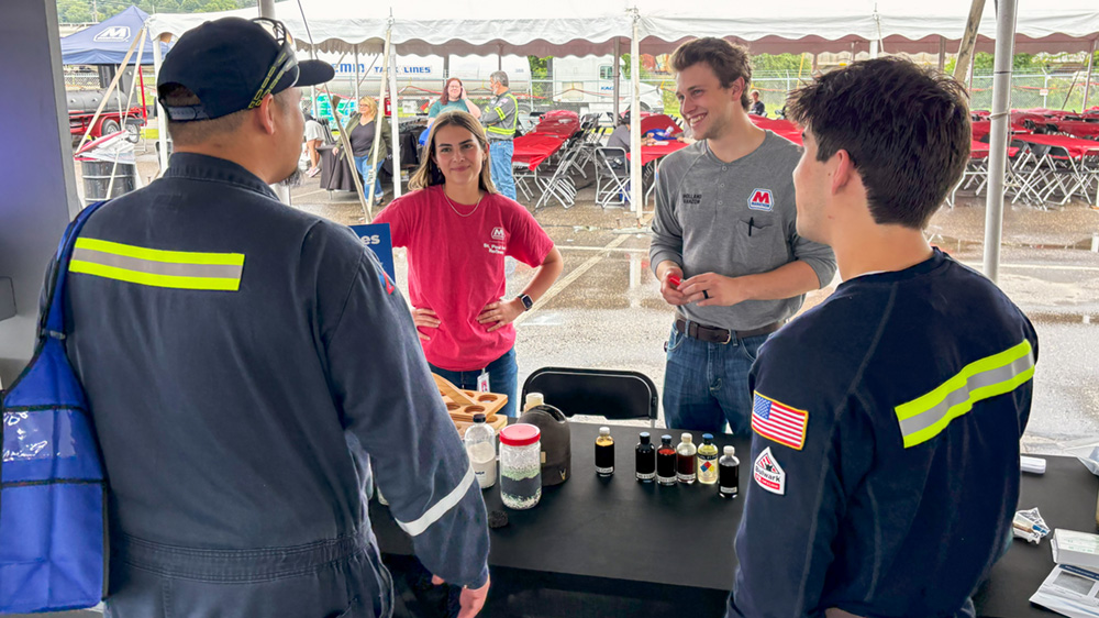 Two people talk with men in blue uniforms at a table with samples on it.
