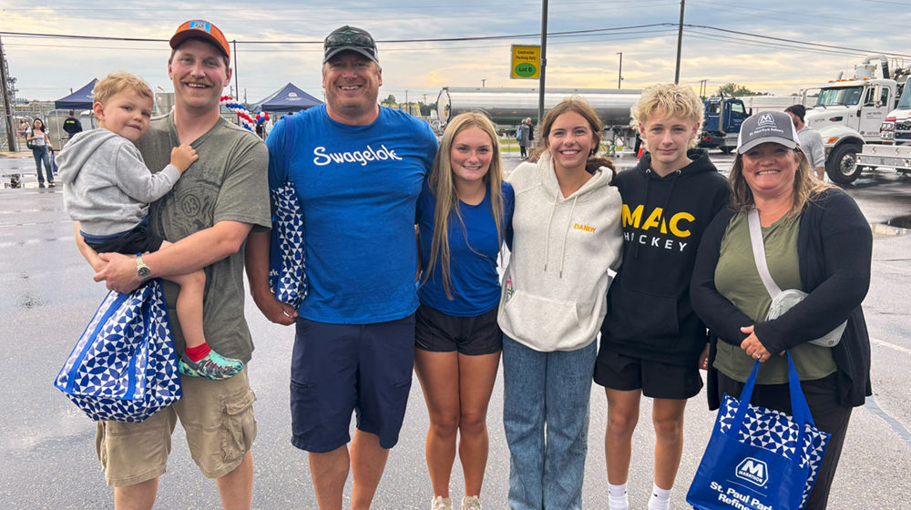 A group of adults and children standing together outdoors on a paved area.