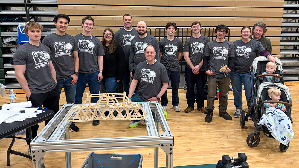 A large group of volunteers and students stand together for a photo inside a school gymnasium.