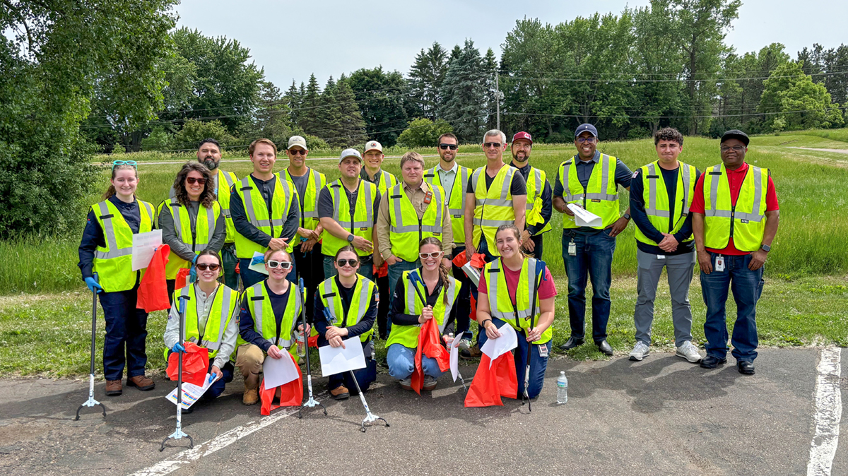 A group of people wearing safety vests stand together during a highway cleanup effort.