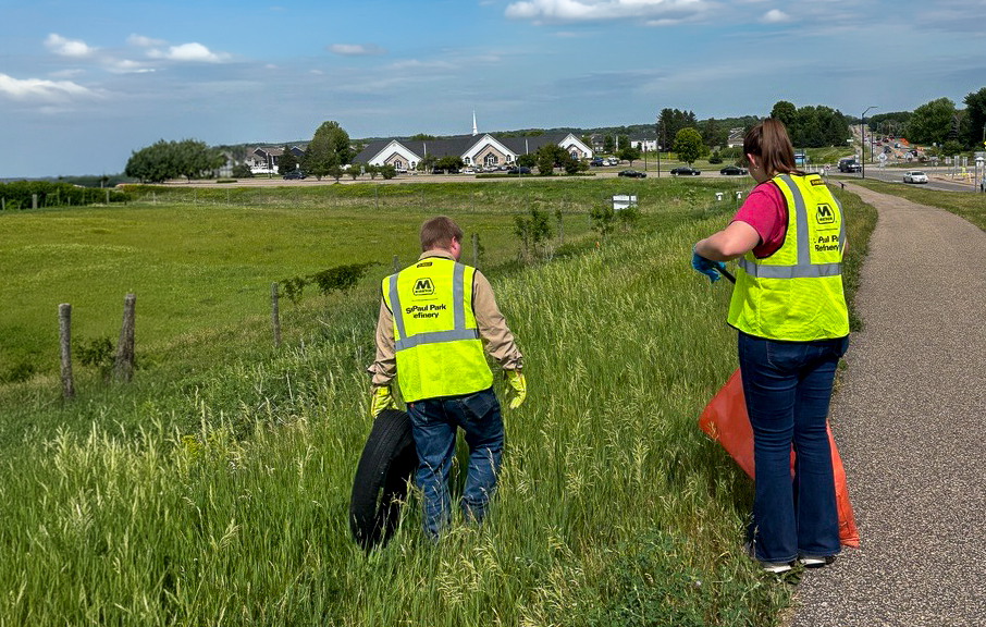 Two people wearing safety vests walk along a roadway collecting trash and debris.