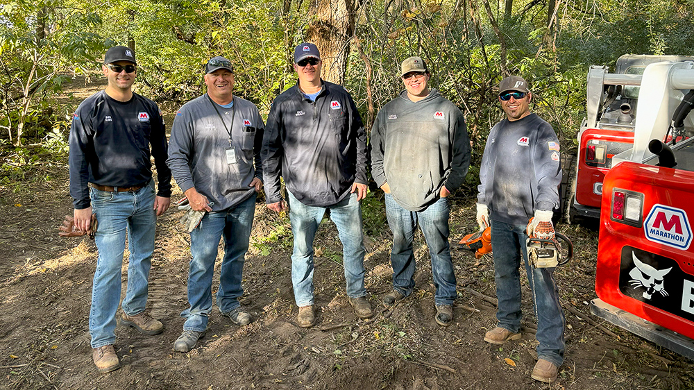 Five people stand together outdoors with trees in the background.
